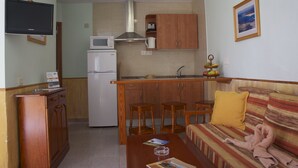 A compact living space with a kitchenette, a sofa, and a television. - Bungalows Castillo Playa (Antigua)