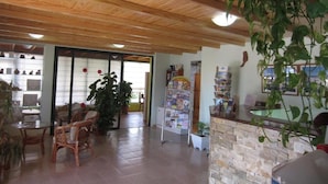 Un área de recepción con techo de madera, muebles de mimbre, mostrador de piedra y un estante con folletos.