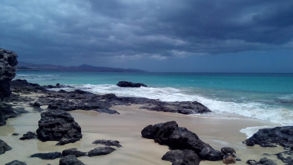 Ein felsiger Strand mit brechenden Wellen unter einem bewölkten Himmel.