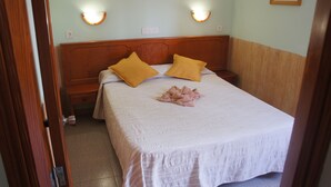A neatly made bed with a wooden headboard, two bedside lamps, and a single pink towel on the bed. - Bungalows Castillo Playa (Antigua)