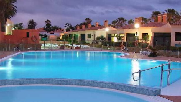 Piscina con borde de azulejos, rodeada de sillas de descanso y una valla.