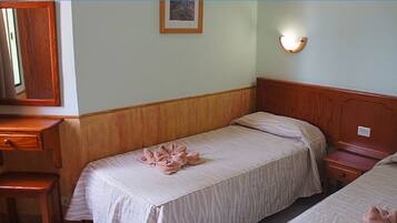 A hotel room with two beds, a wooden headboard, a small wooden desk with a drawer, a mirror, and a wall-mounted light fixture.
