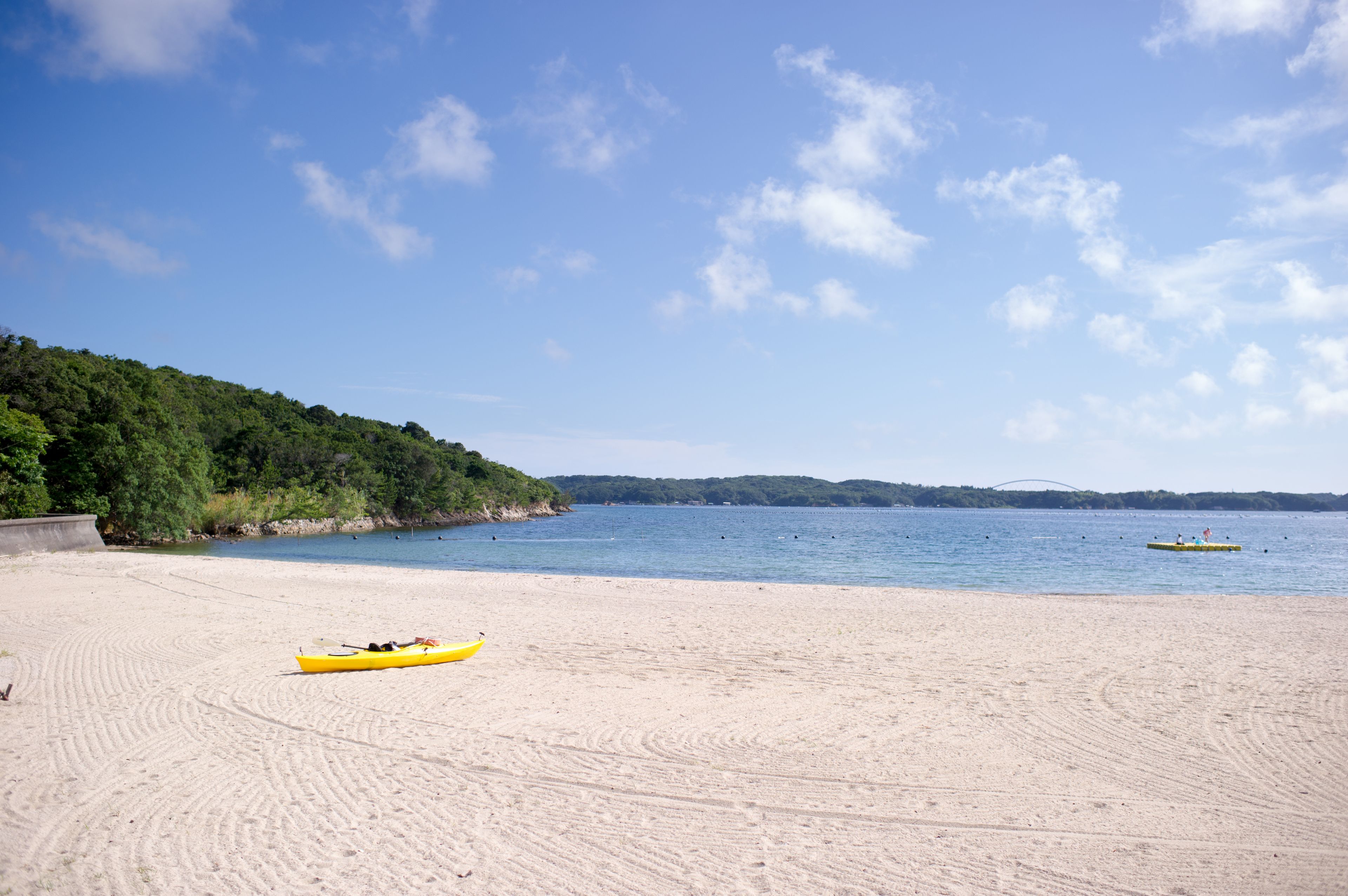 Uma praia arenosa com um caiaque amarelo e um barco pequeno na água.