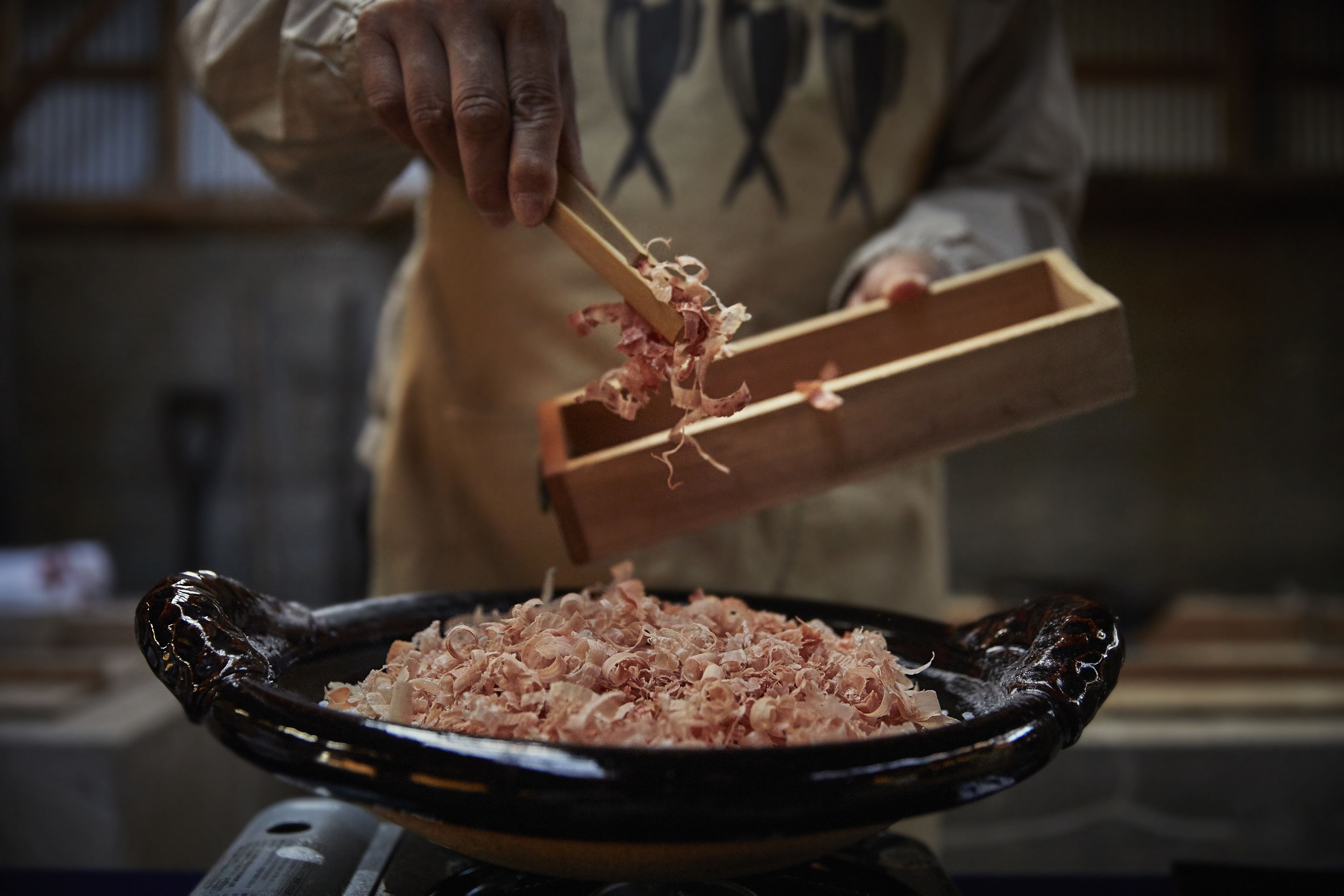A person using chopsticks to transfer shredded meat into a black pan.