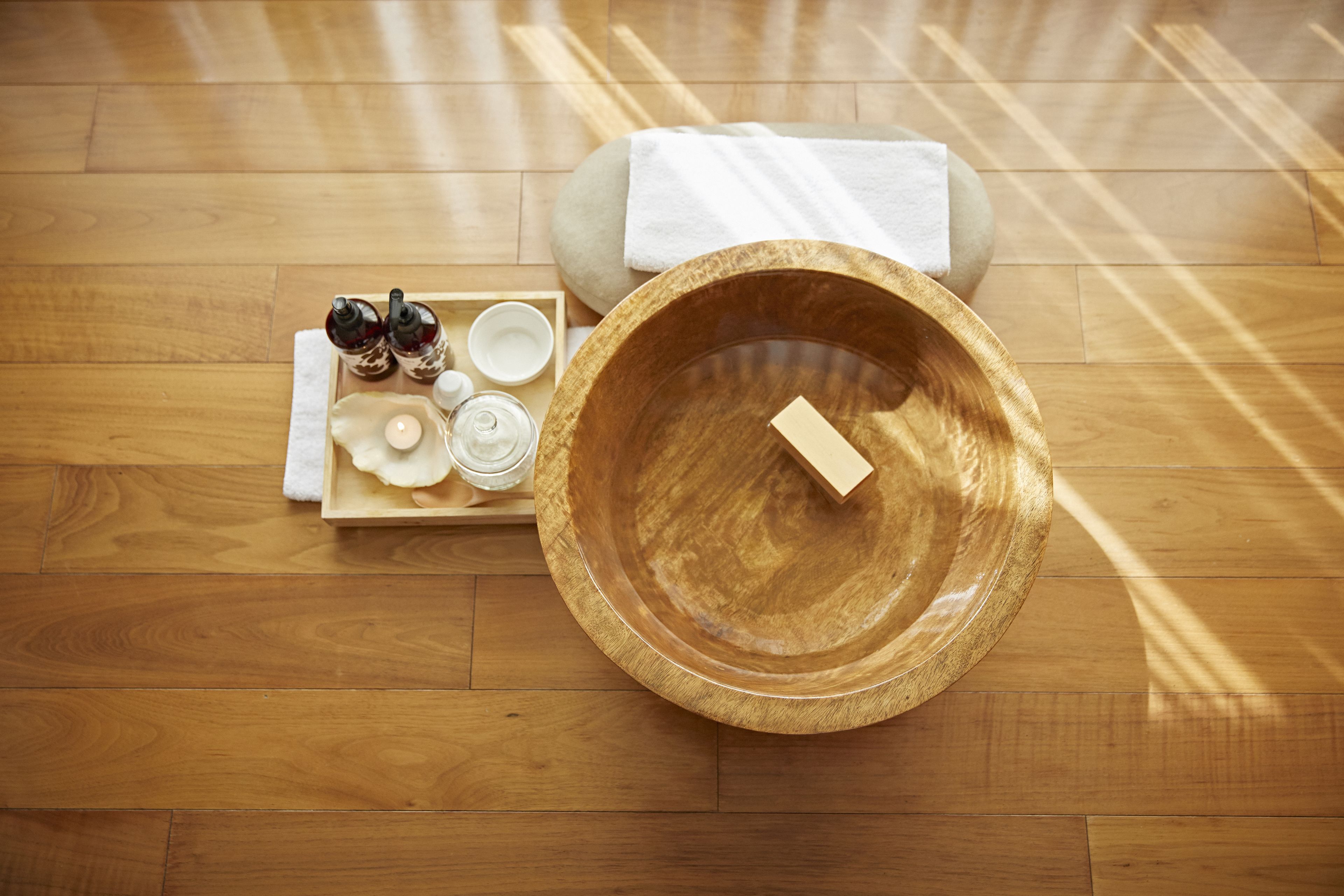 A wooden floor with a wooden bowl and a tray of toiletries.