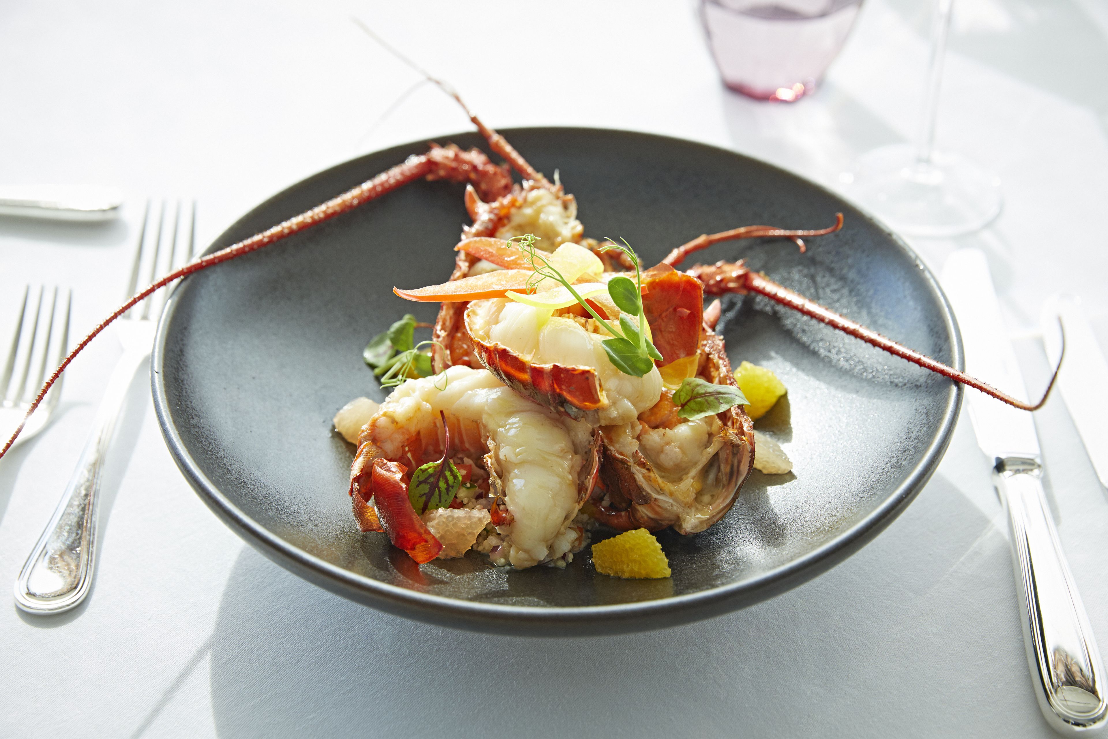 A plate of lobster with vegetables and a glass of wine on a table.