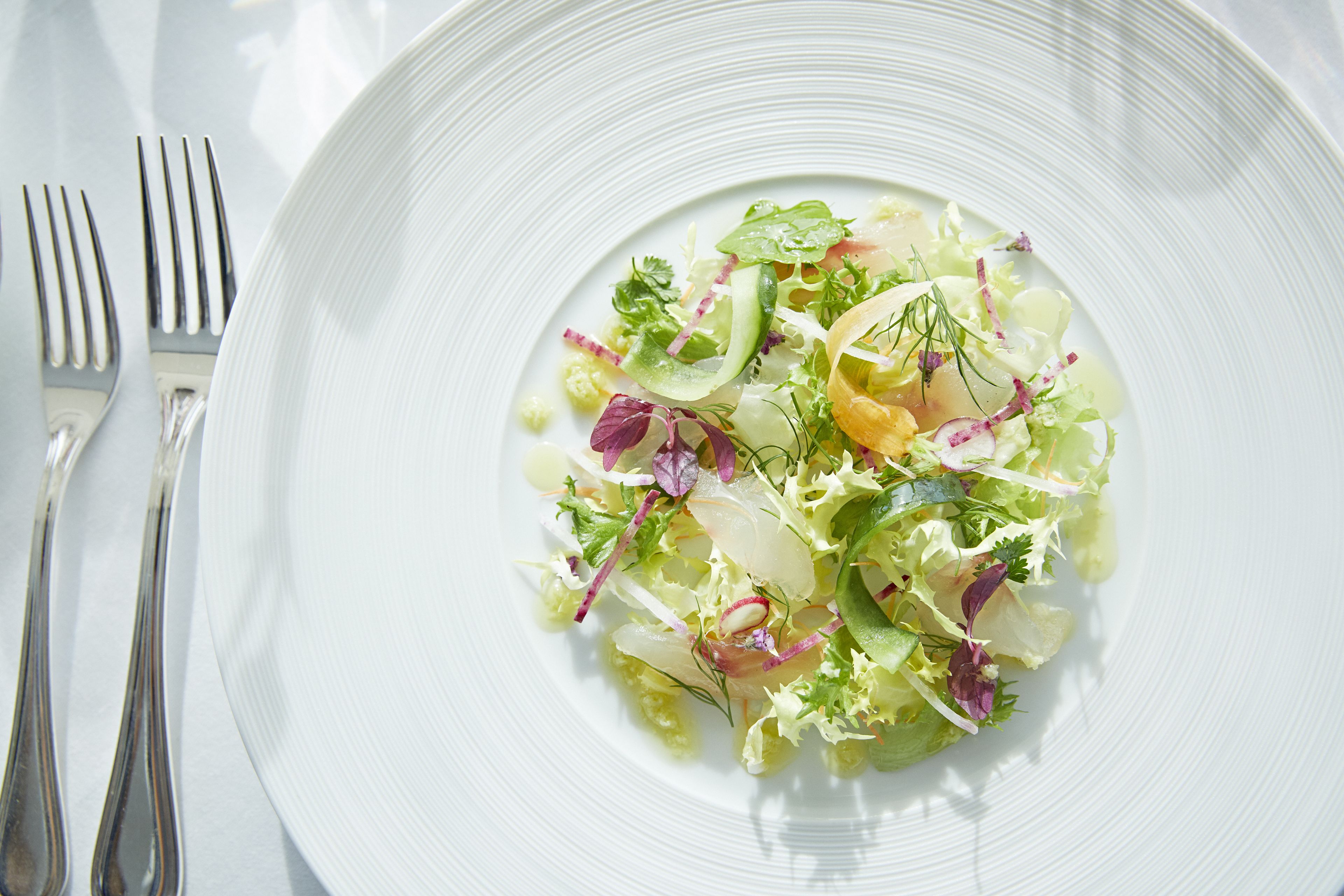 A white plate with a salad on a table.