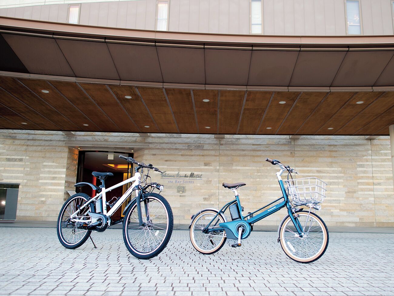Two bicycles parked in front of a building with a brick facade and a sign that reads "The Bay Suites."