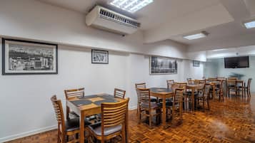 Een eetruimte met houten tafels en stoelen, airconditioning en ingelijste foto's aan de wanden.
