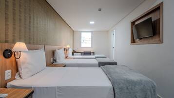 A hotel room with two beds, a desk, a chair, a TV mounted on the wall, and a window providing natural light.