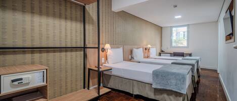 A hotel room with two beds, a wooden floor, a small desk, and a window.