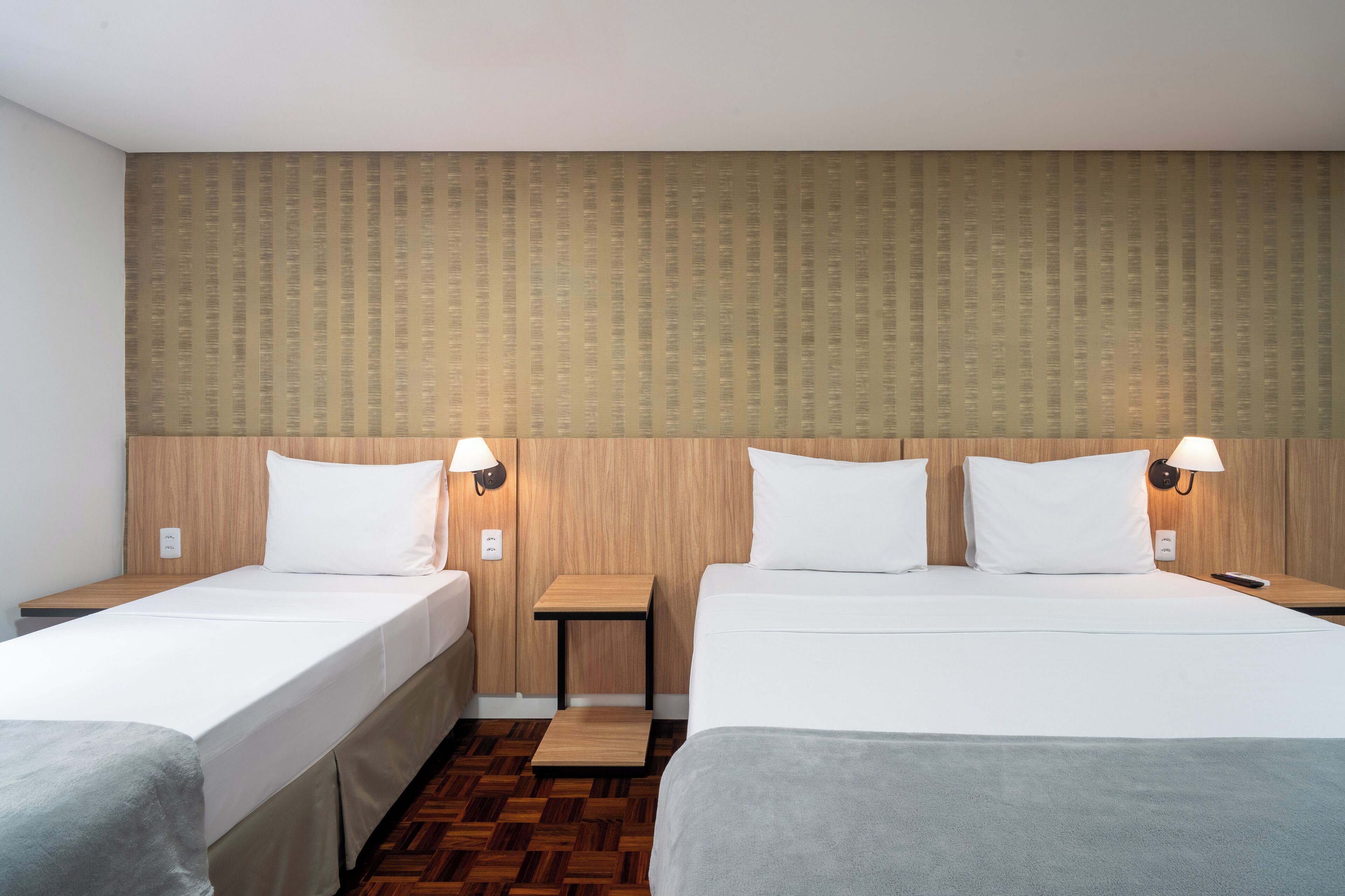 Habitació d'hotel amb dos llits individuals, panell de capçalera de fusta i tauletes de nit amb làmpades.