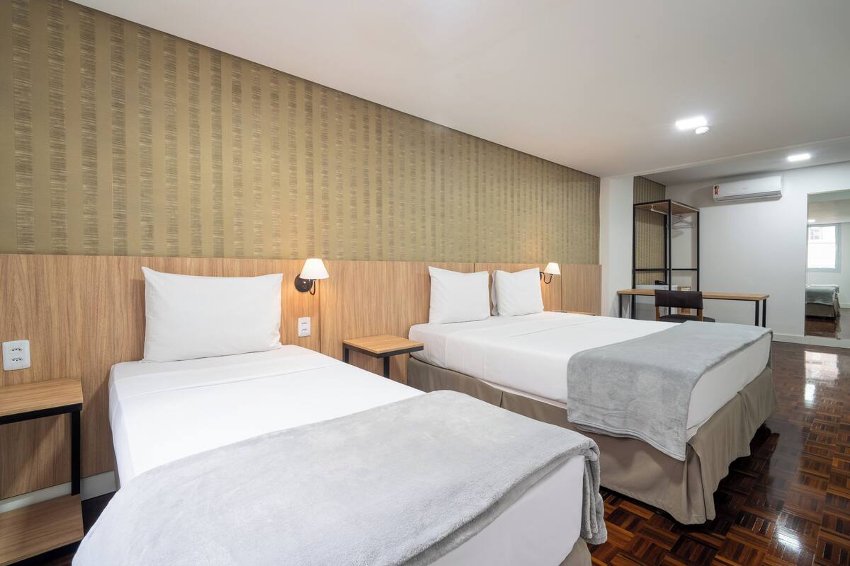 A hotel room with two beds, wooden headboards, a small table, and a chair.