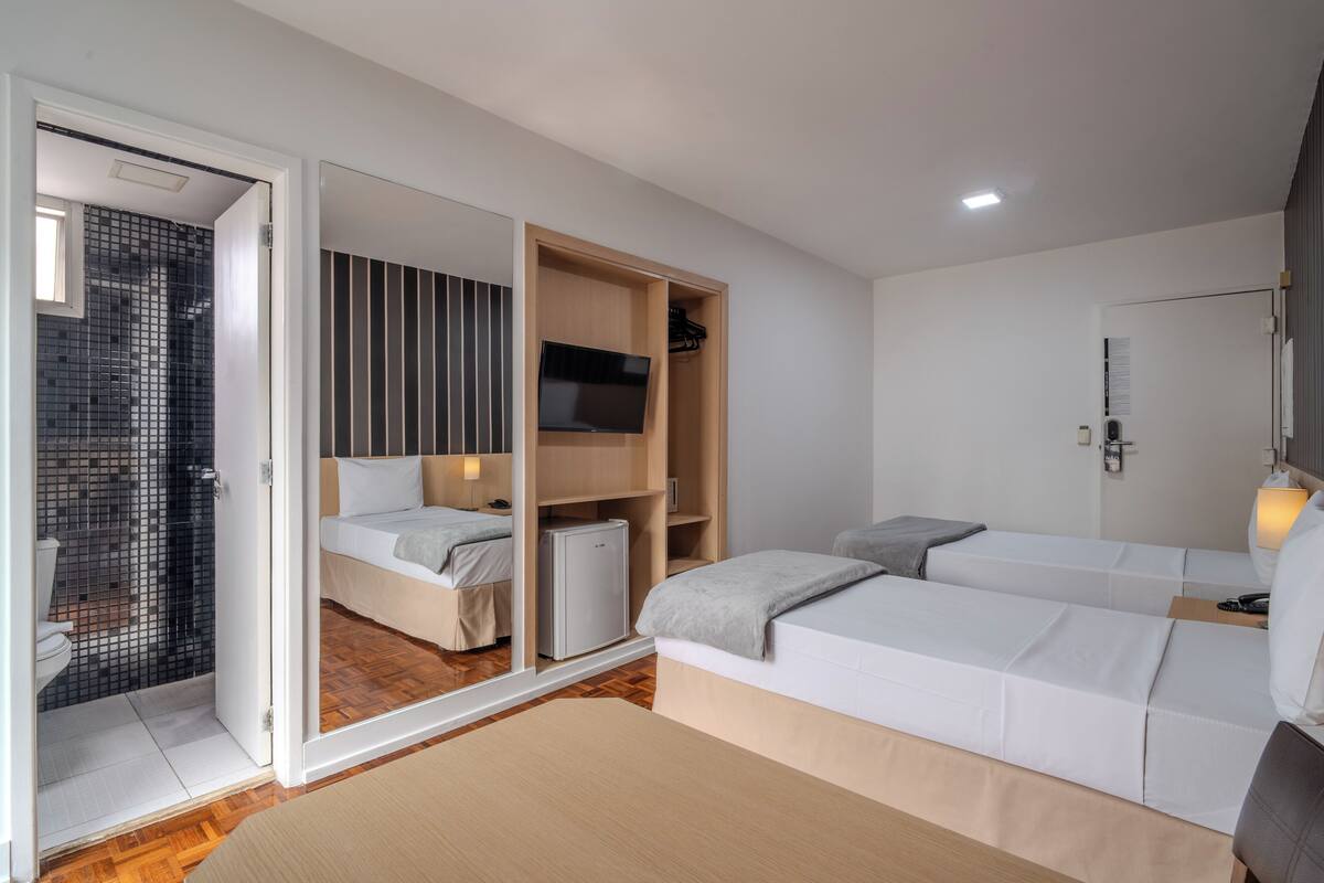 A modern bedroom with two beds, a TV, and a wardrobe.