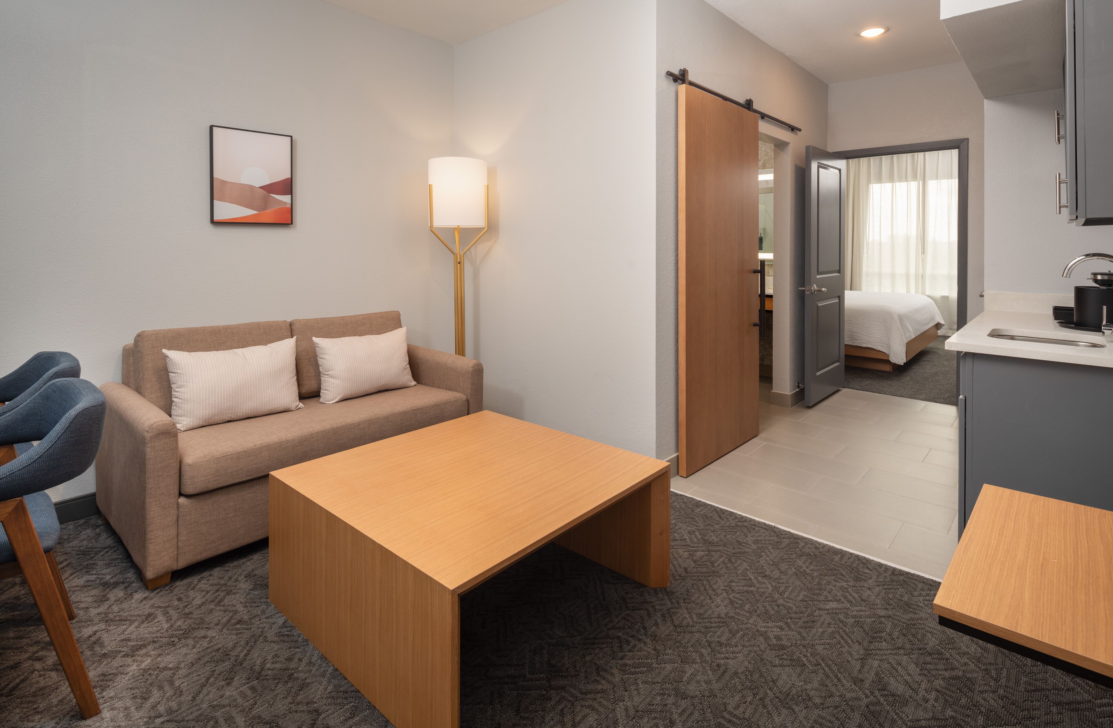 Een moderne hotelkamer met een bank, een houten bijzettafeltje, een bureau en een kitchenette.