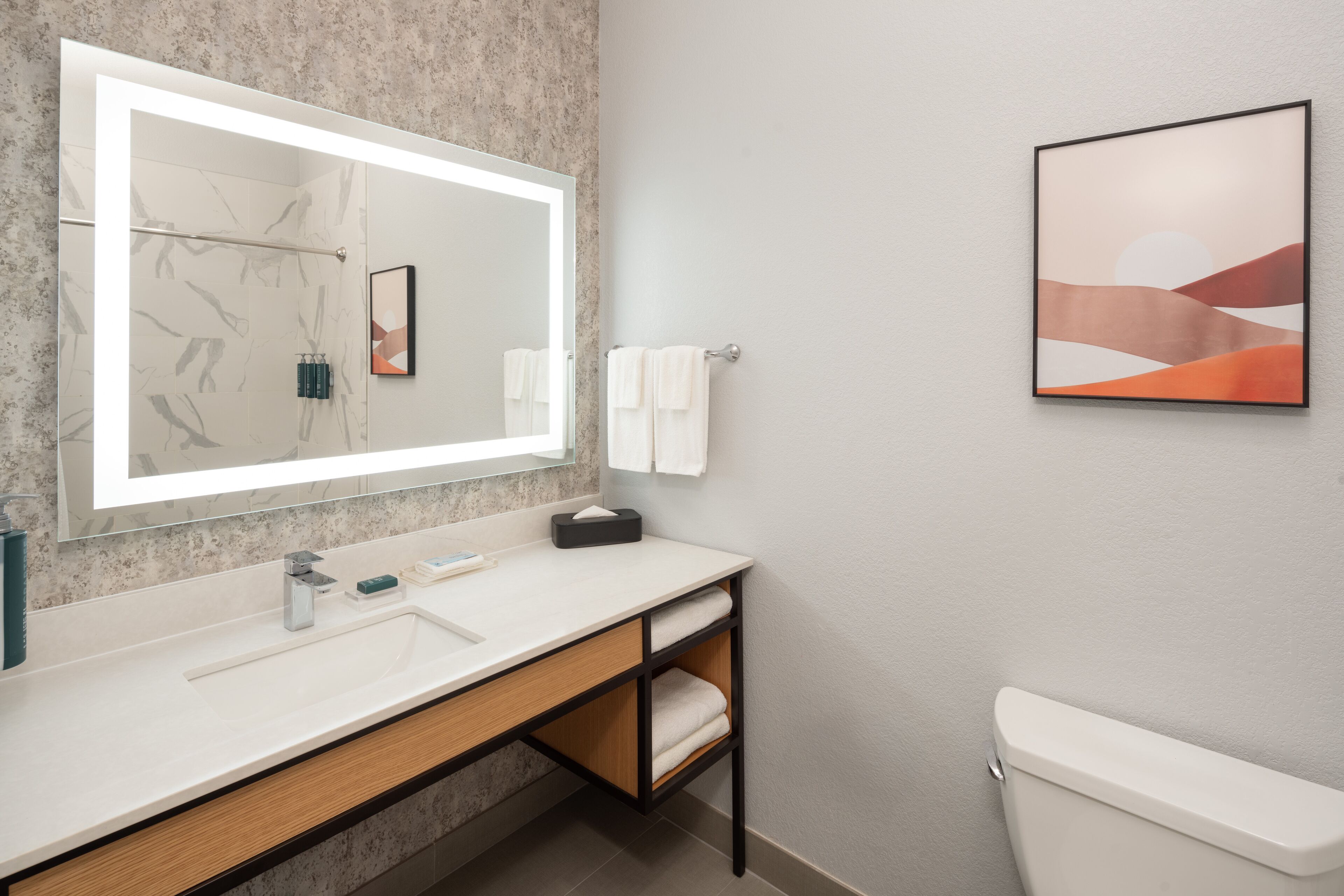 Un baño moderno con un espejo grande, un lavamanos blanco y un inodoro.