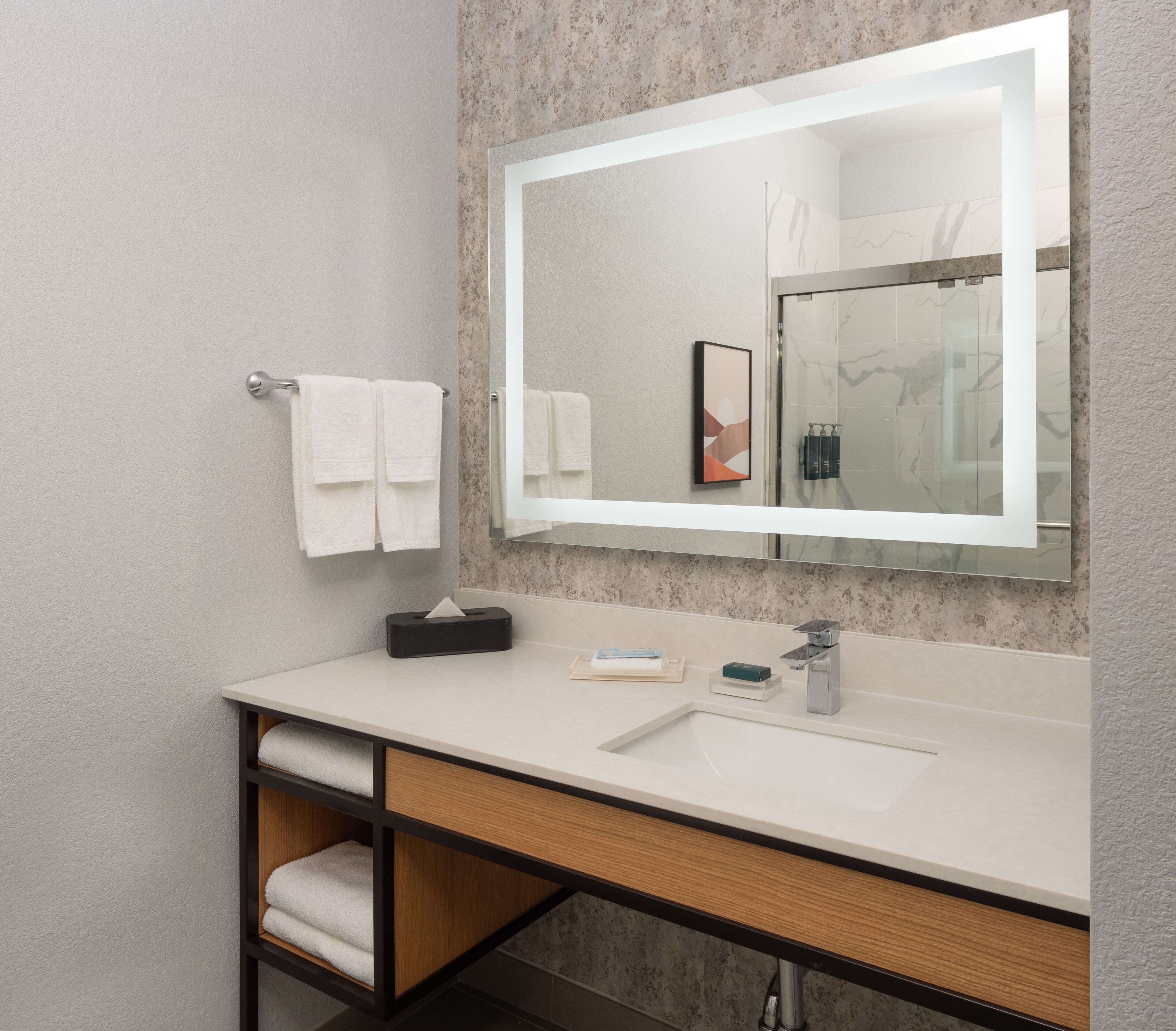 A modern bathroom with a large mirror, white sink, and a towel rack with two towels.