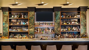 A bar area with multiple shelves of liquor bottles, a flat-screen TV above the bar, and four bar stools. - DoubleTree by Hilton Houston Westchase (Houston)