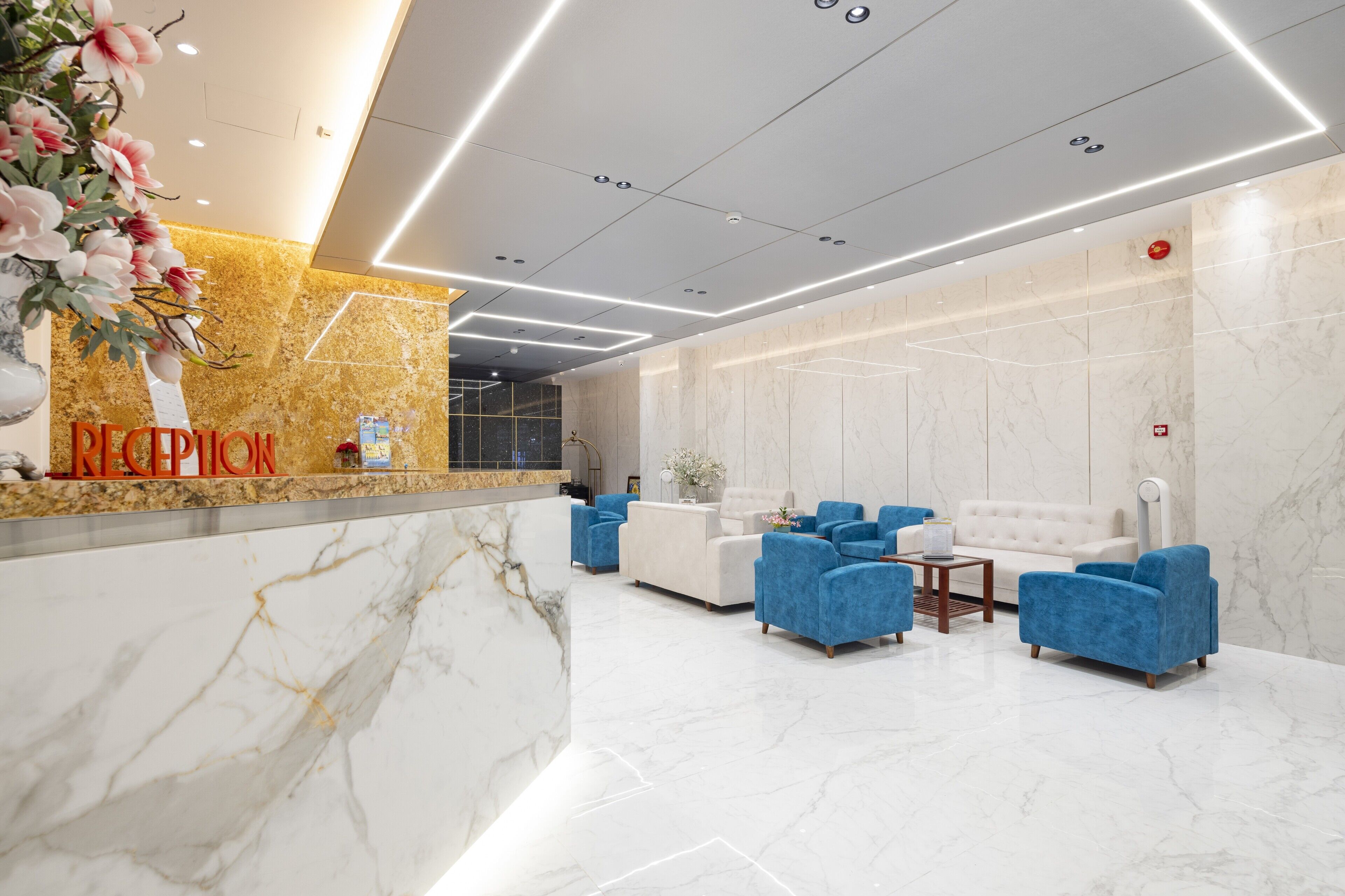 A reception area with a marble reception desk, blue armchairs, and a white sofa.