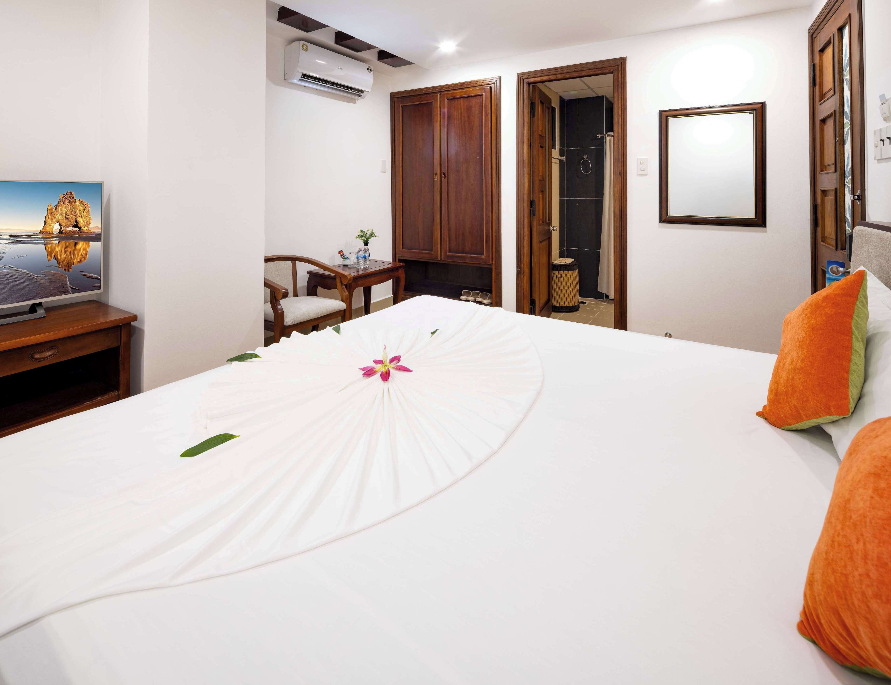 Une chambre d’hôtel avec un lit, un téléviseur posé sur un meuble en bois, une armoire en bois et une salle de bain visible à travers une porte ouverte.