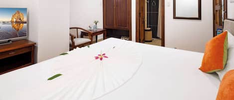 A hotel room with a bed, a TV on a wooden stand, a wooden wardrobe, and a bathroom visible through an open door.