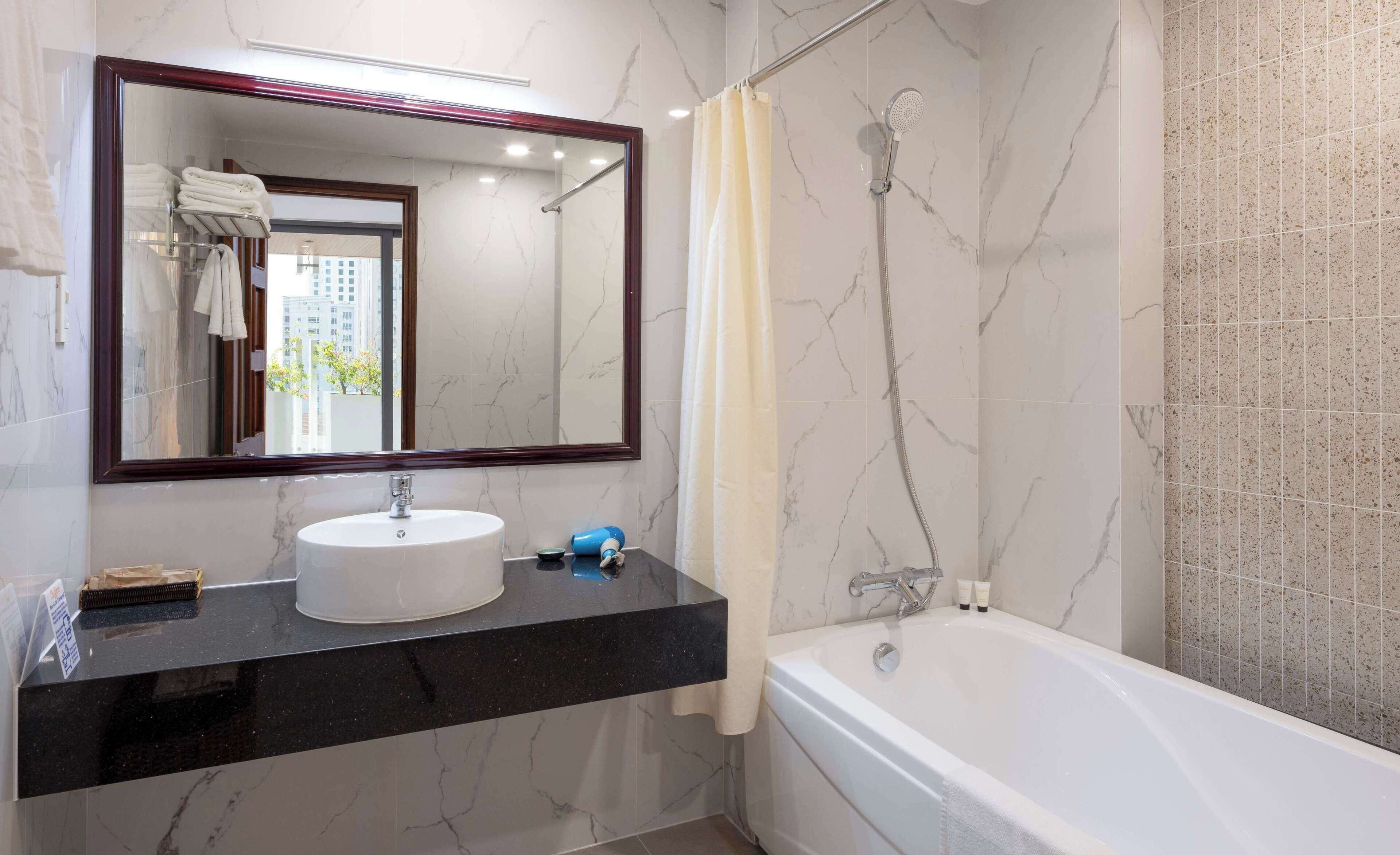 Une salle de bain avec un mur en marbre, un lavabo blanc, un grand miroir, une douche et une baignoire.