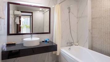 A bathroom with a marble wall, a white sink, a large mirror, a shower, and a bathtub.