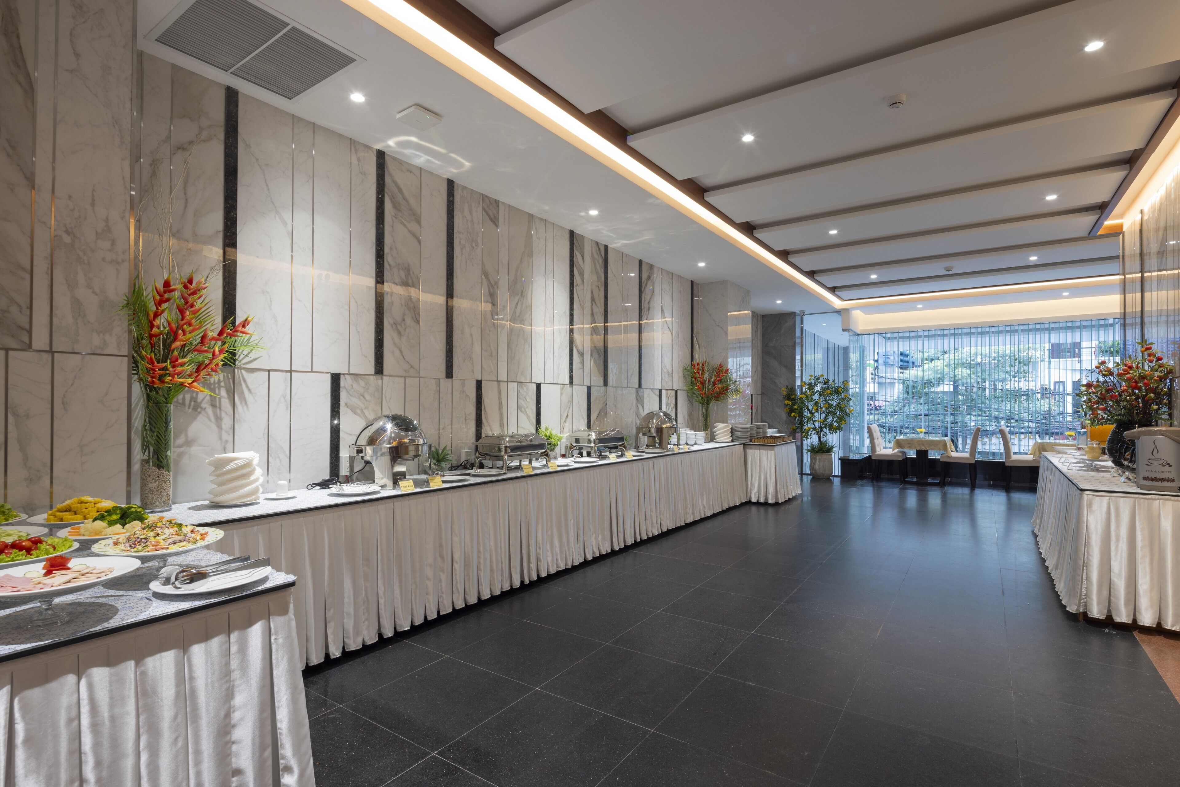 En moderne hotelrestaurant med marmorvægge, et buffetbord og et siddeområde med stole og et bord.