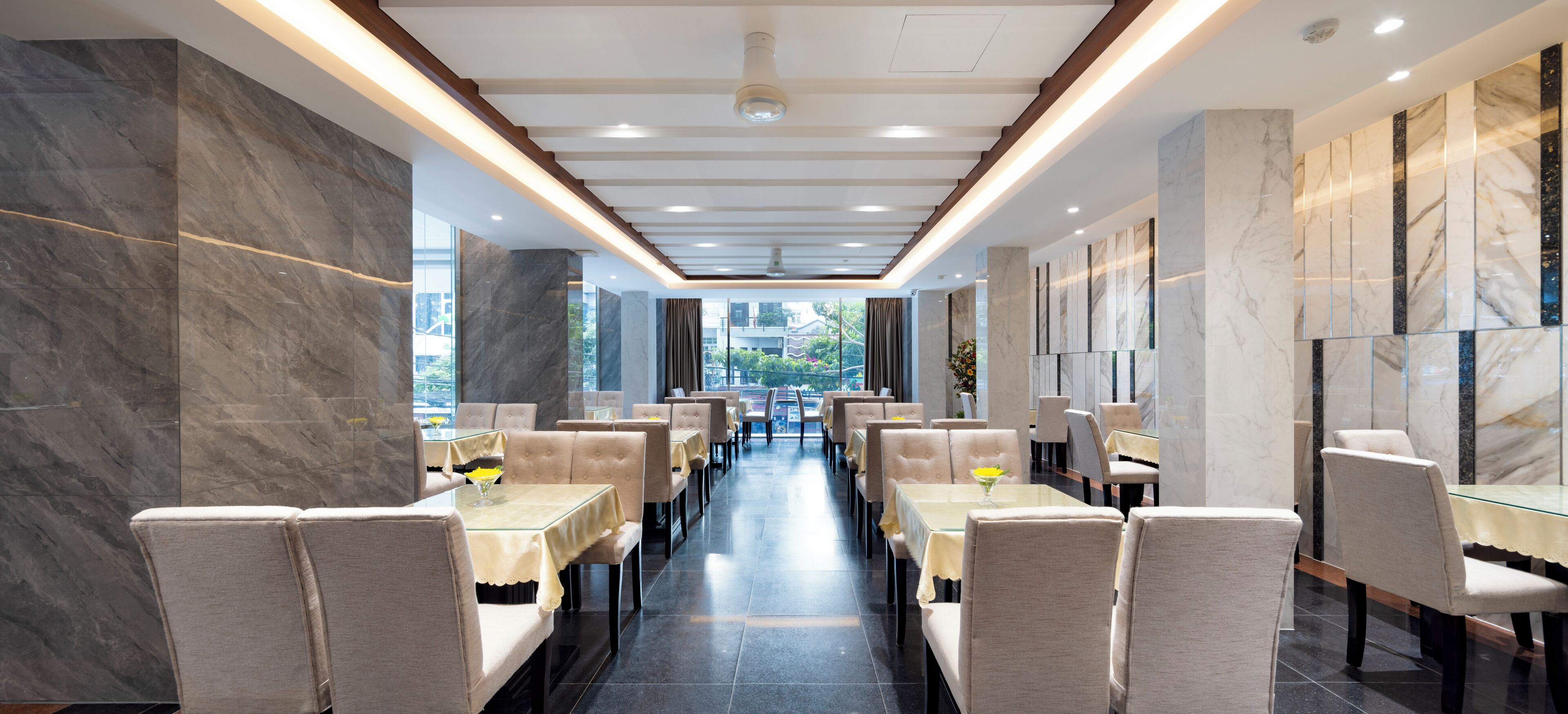 A modern restaurant with a long, narrow layout, featuring marble walls and ceiling, and a central aisle with tables and chairs.