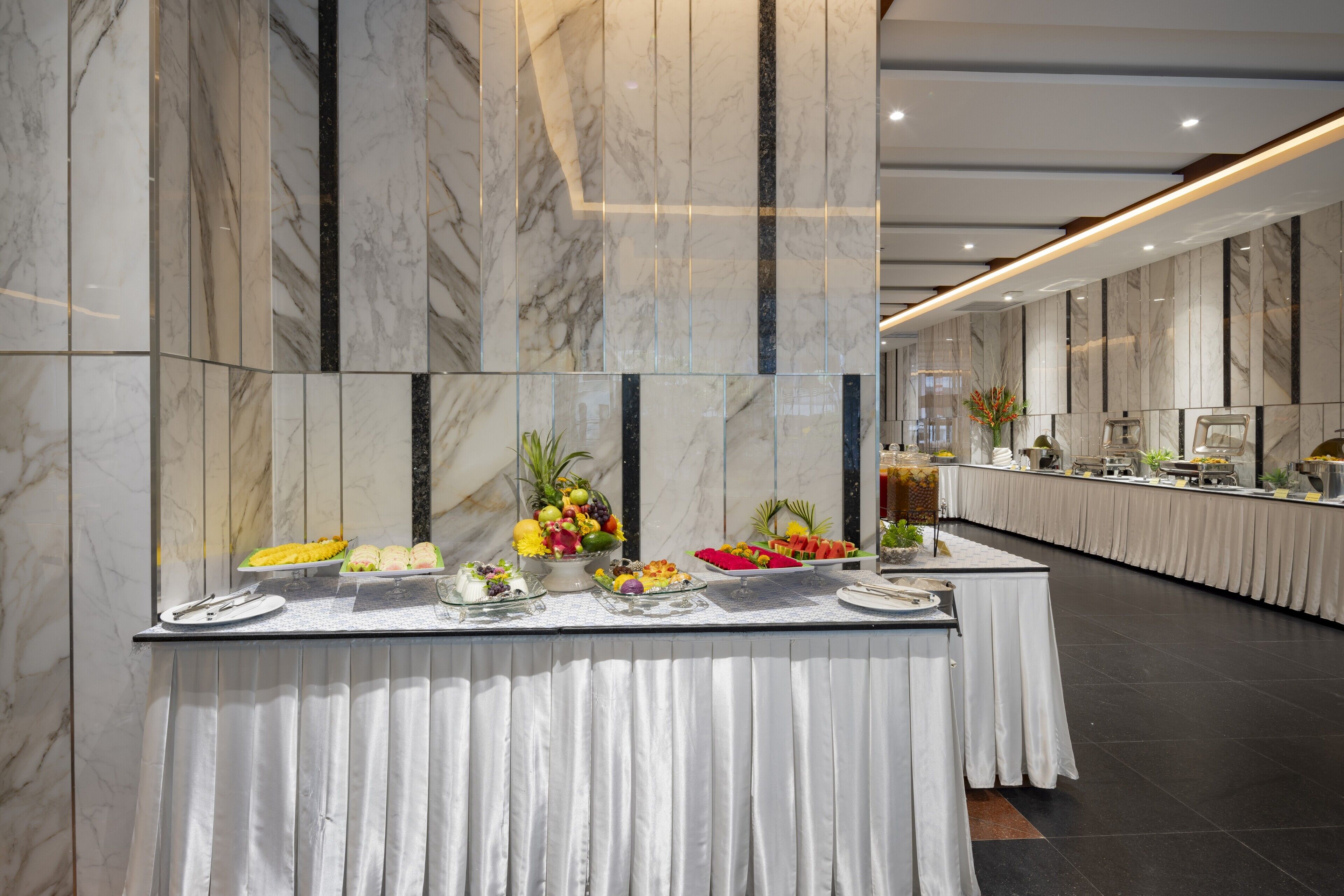 A buffet setup with various food items and a long table against marble walls.