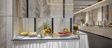 A buffet setup with various food items and a long table against marble walls.