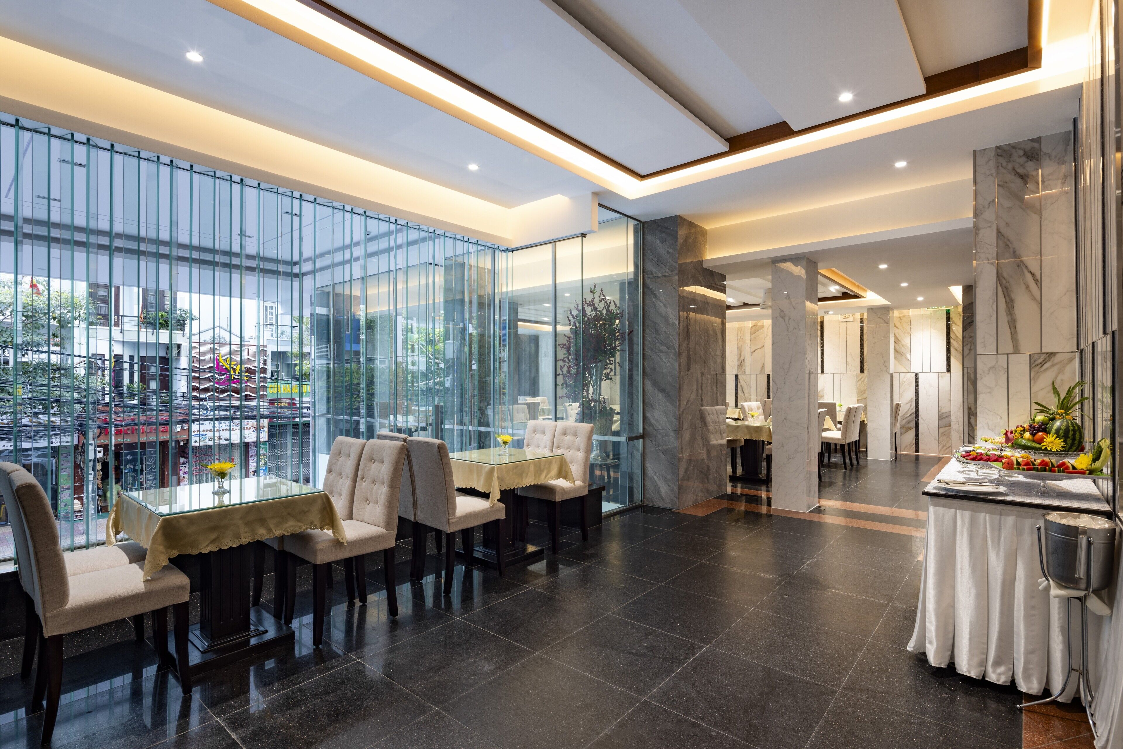 A modern dining area with glass partitions, a marble reception desk, and a view of the cityscape.