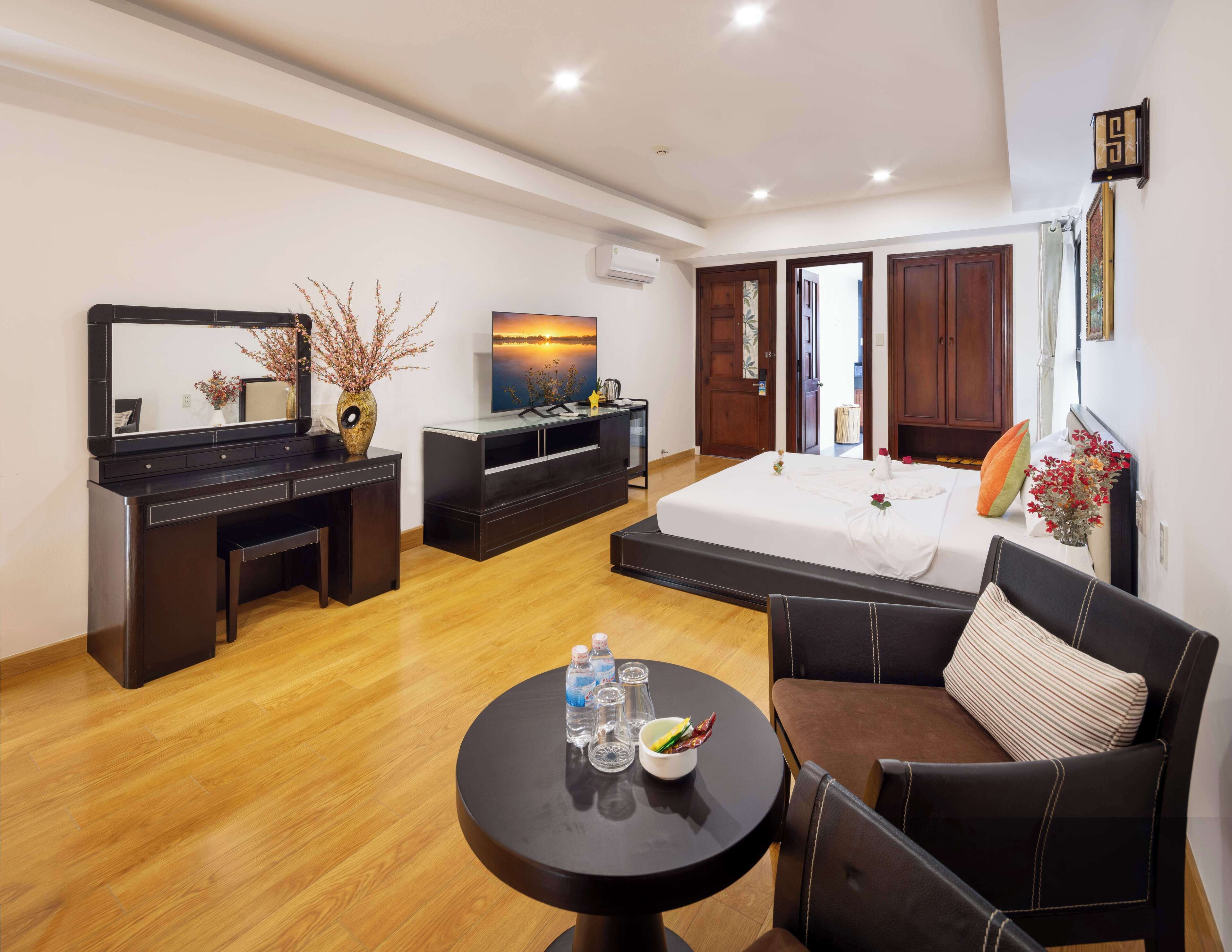 Une chambre d’hôtel moderne équipée d’un lit, d’un bureau, d’une télévision, d’un canapé et d’une petite table sur laquelle se trouvent des bouteilles d’eau.