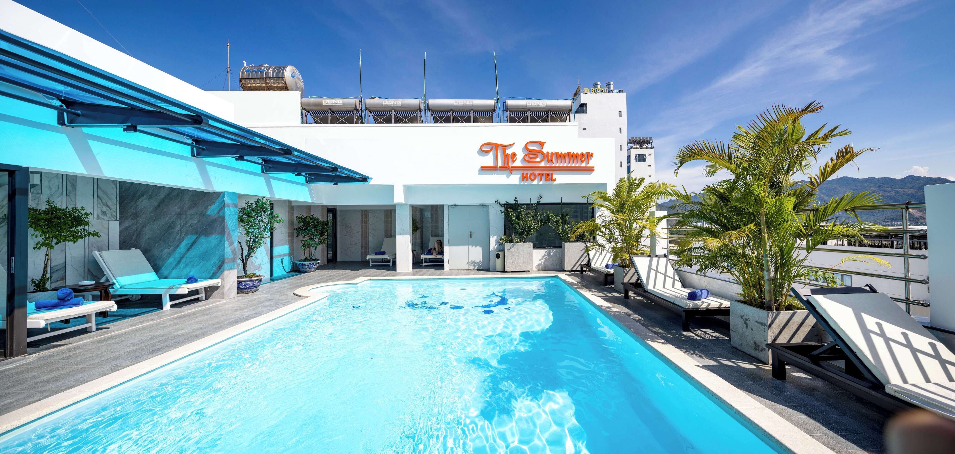 Un hotel con piscina en la azotea, sillas de descanso y vistas a las montañas.