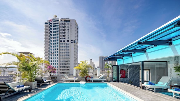 Una piscina en la azotea con agua azul cristalina, sillas de descanso y vista panorámica a la ciudad.