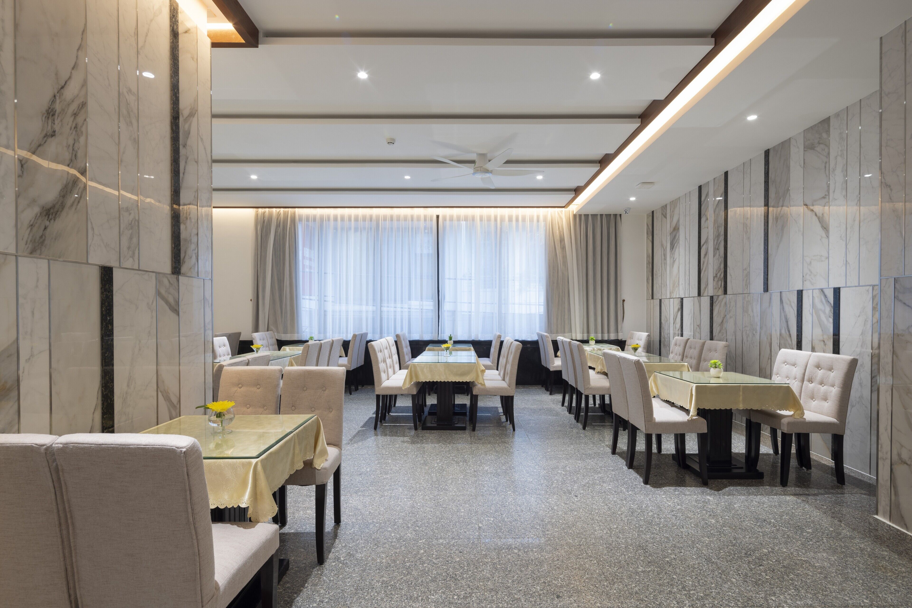 Comedor de hotel con paredes de mármol, una mesa central rodeada de sillas y un ventilador de techo.