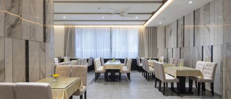 A hotel dining area with marble walls, a central table surrounded by chairs, and a ceiling fan.
