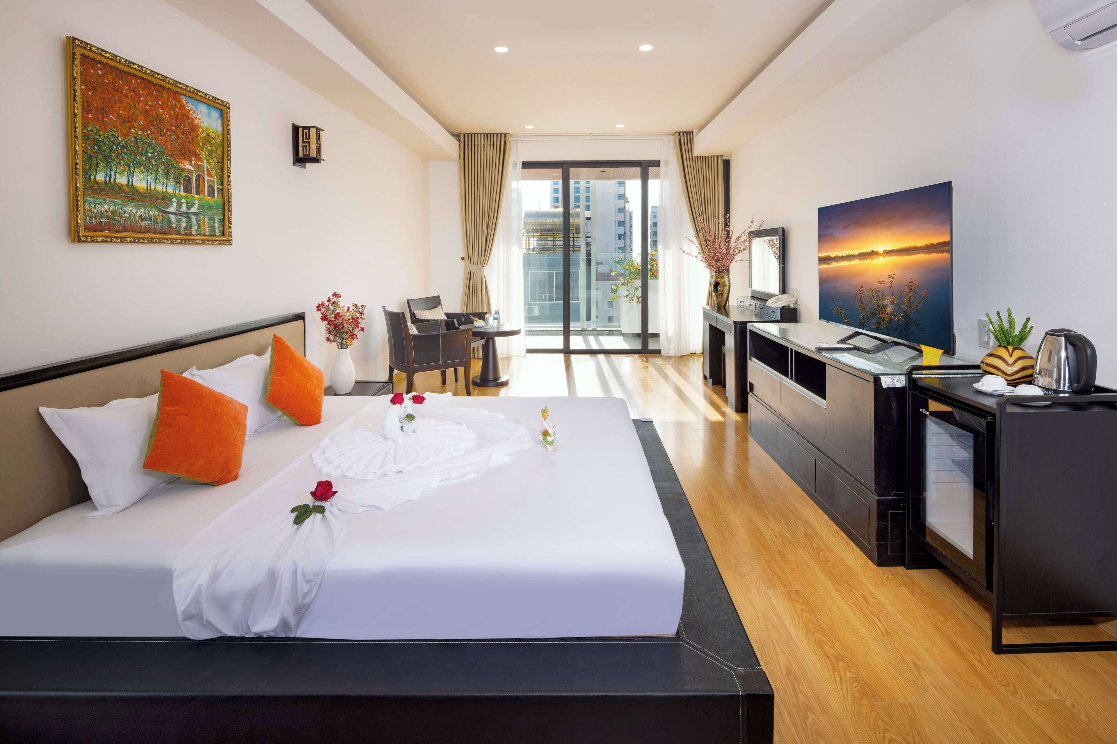 A hotel room with a large bed, a desk, a chair, a TV, and a view of the city through the window.