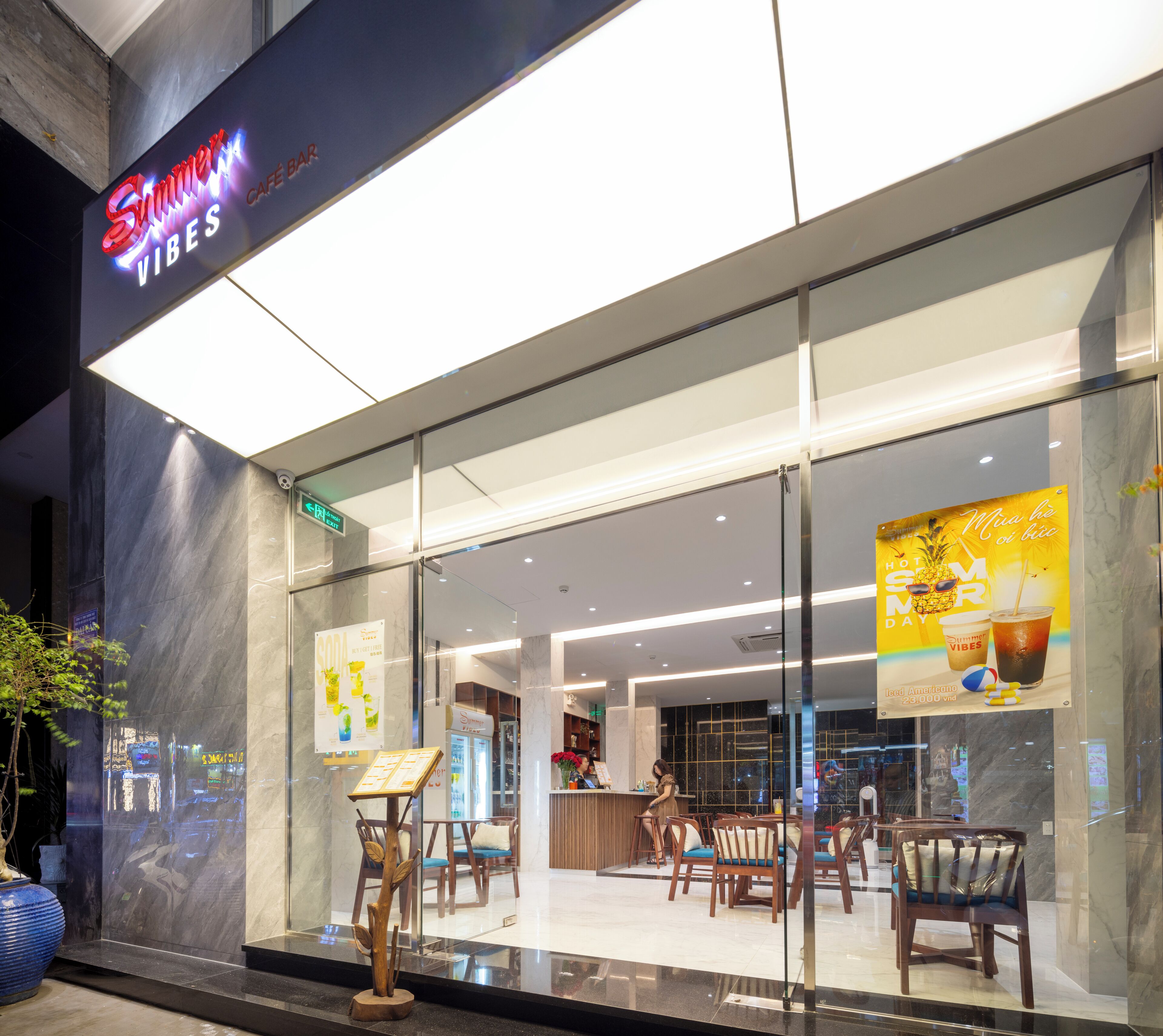 A modern cafe with a glass facade, wooden chairs, and a neon sign.