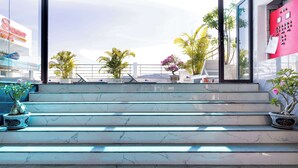 Un conjunto de escaleras de mármol que conducen a un balcón con plantas en macetas y vistas a palmeras y un edificio con un cartel.