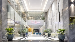 Un moderno vestíbulo de hotel con una recepción central, paredes de vidrio y plantas en macetas.