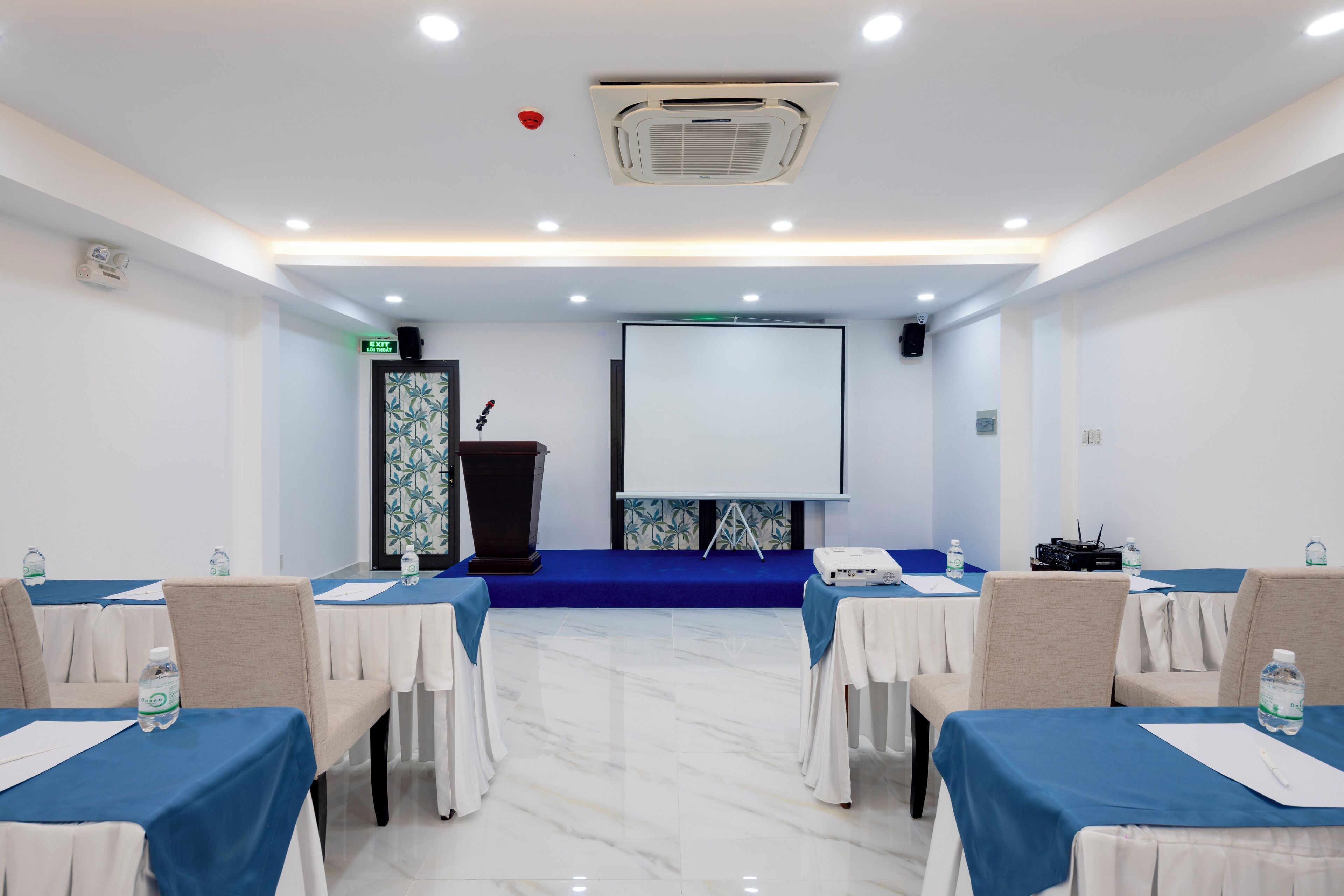 A conference room with a blue carpet, white tables, and chairs.