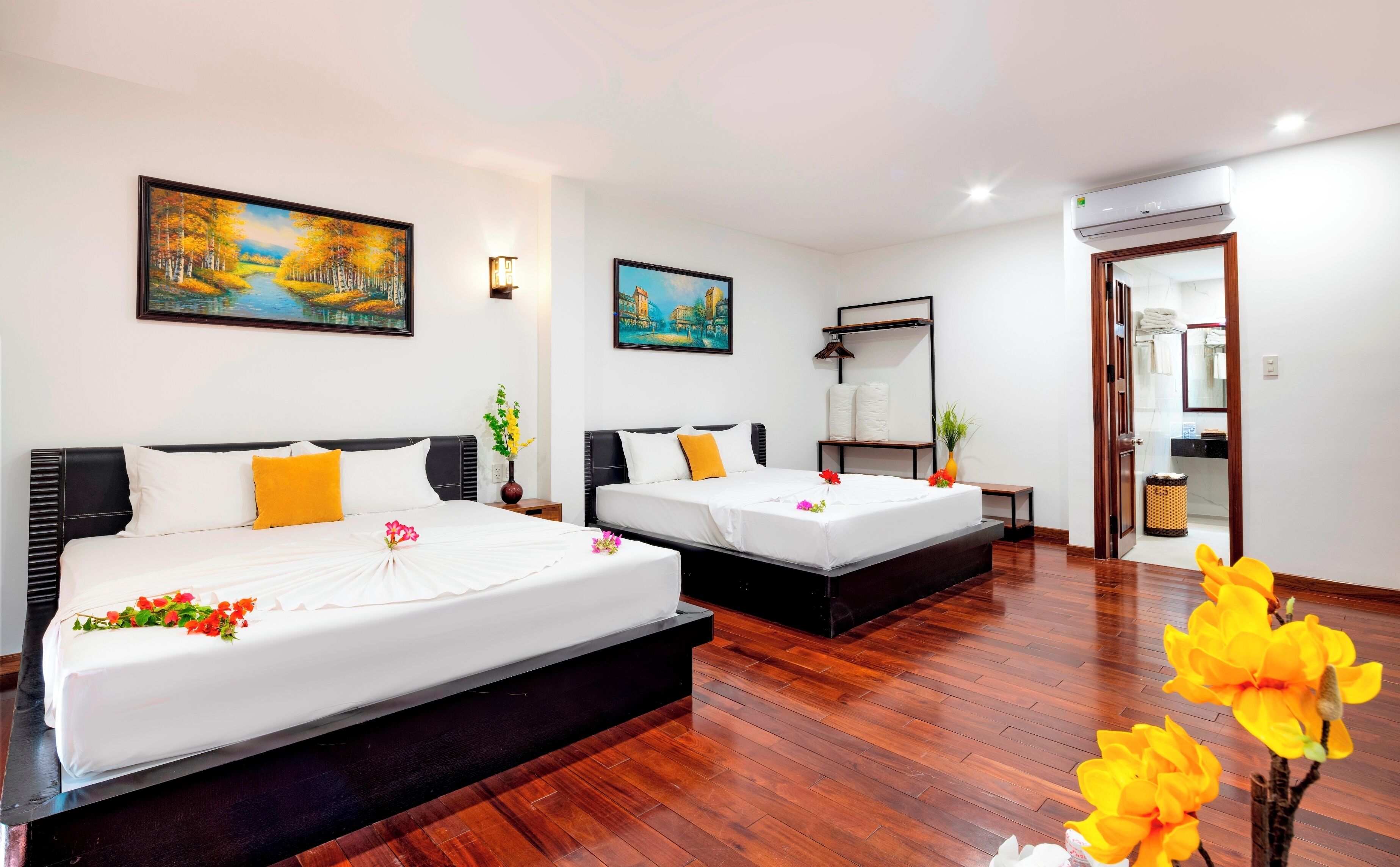 A hotel room with two beds, a painting of a landscape, a mirror, and a wooden floor.