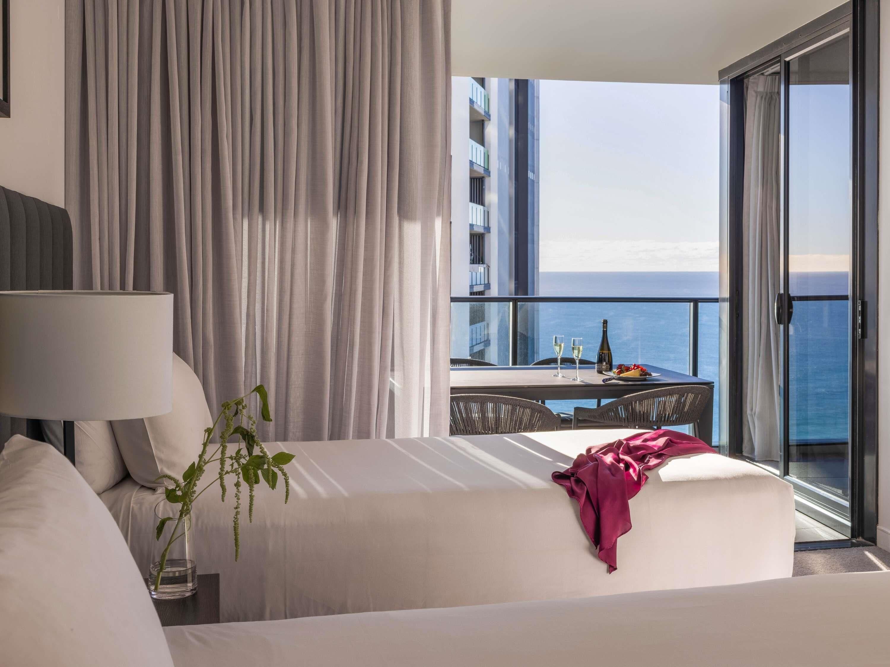 A hotel room with a balcony, a bed, a table with drinks, and a view of the sea.