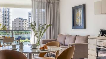 A modern living room with a sofa, chairs, a dining table, a coffee machine, and a view of the cityscape.