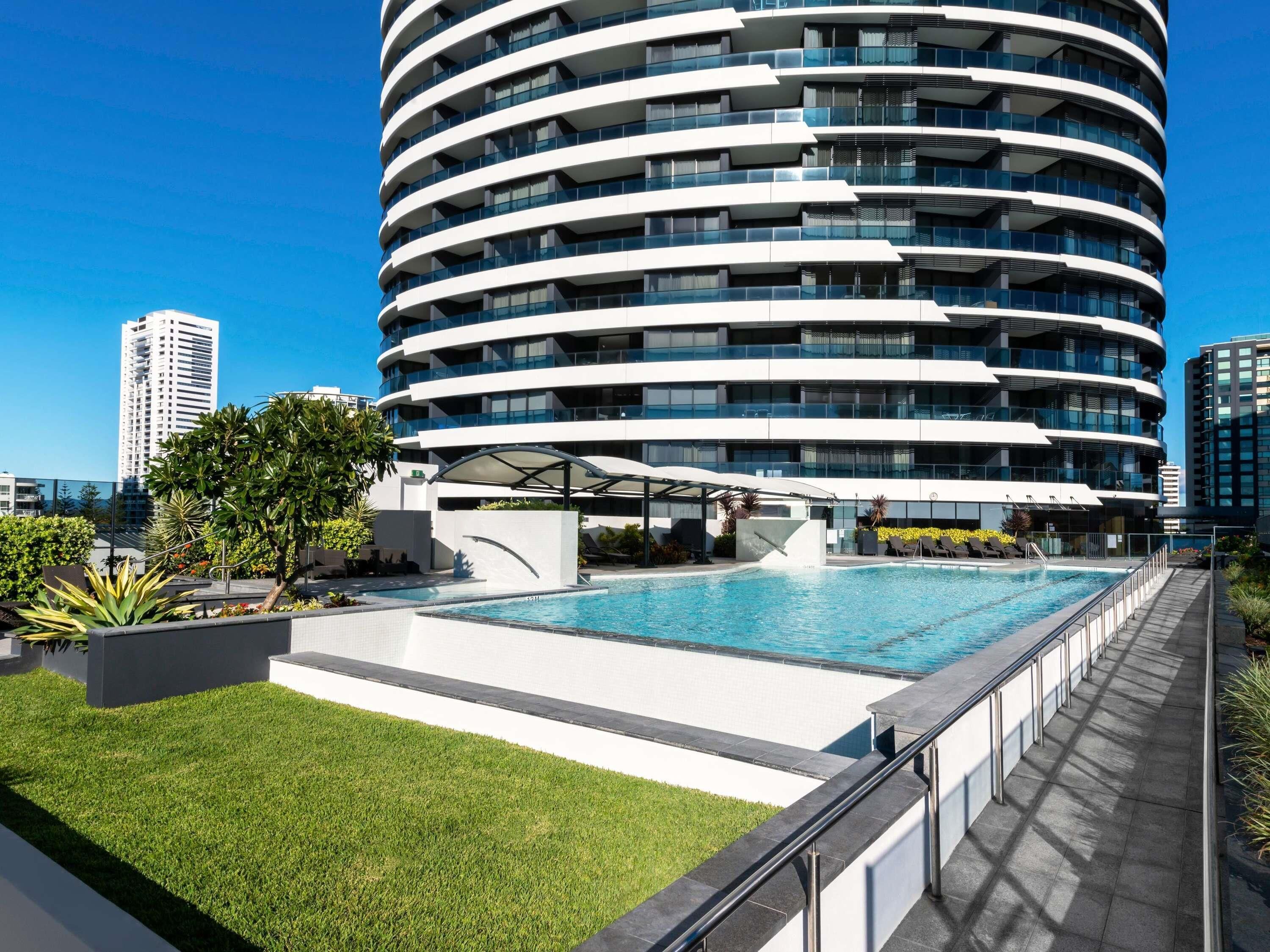 A modern building with a circular design, a rooftop pool, and a well-maintained lawn.