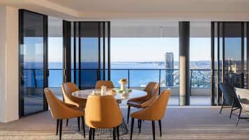 Un comedor moderno con una mesa dispuesta para cuatro, ventanas amplias que ofrecen vistas a la ciudad y al mar, y un balcón con vista al mar.