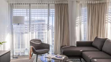Ein modernes Hotelzimmer mit einer Couch, einem Sessel und einem runden Couchtisch mit einer Zeitschrift und einem Glas Wasser.