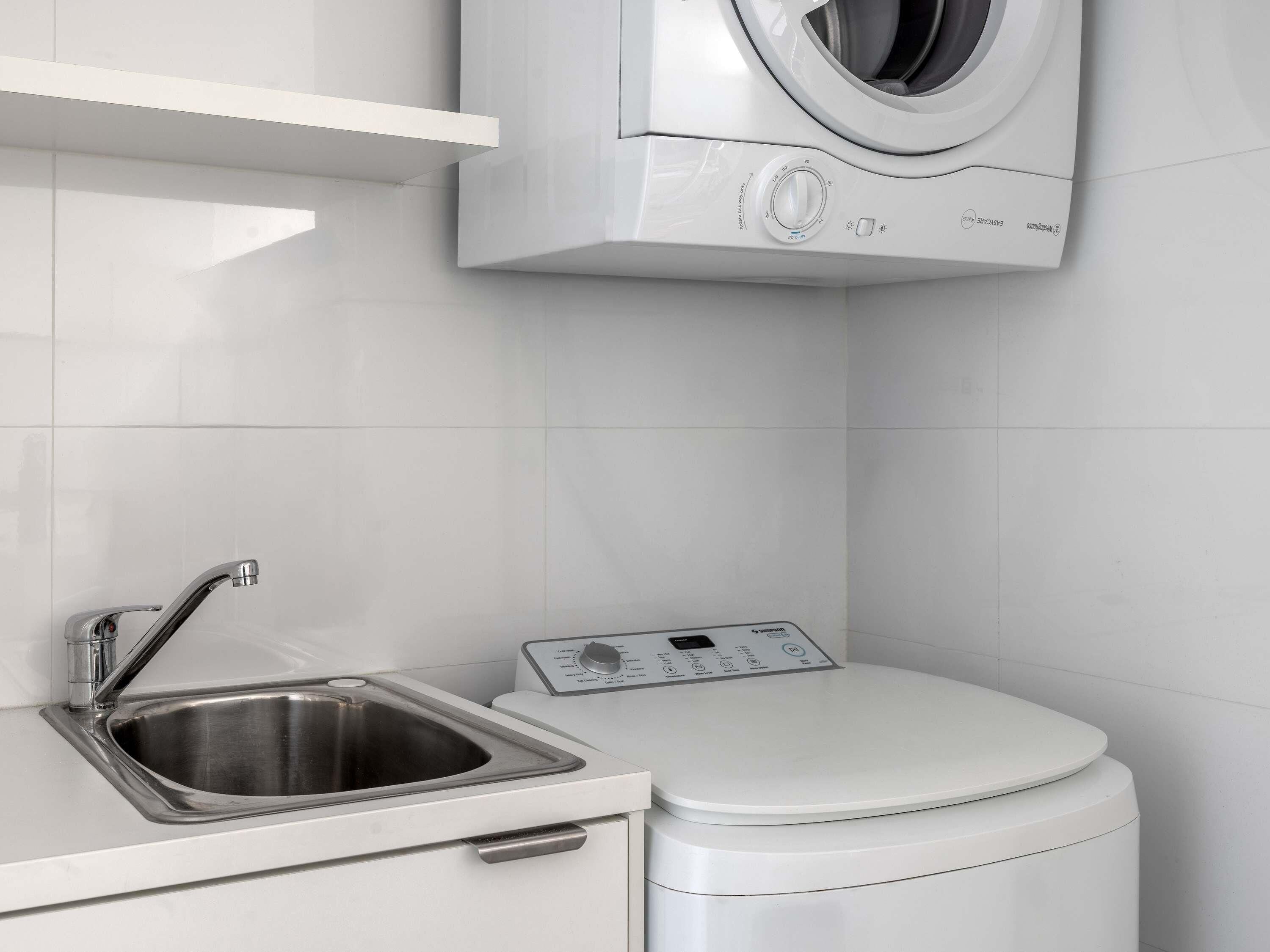 A compact laundry area with a washing machine, a stainless steel sink, and a toilet.