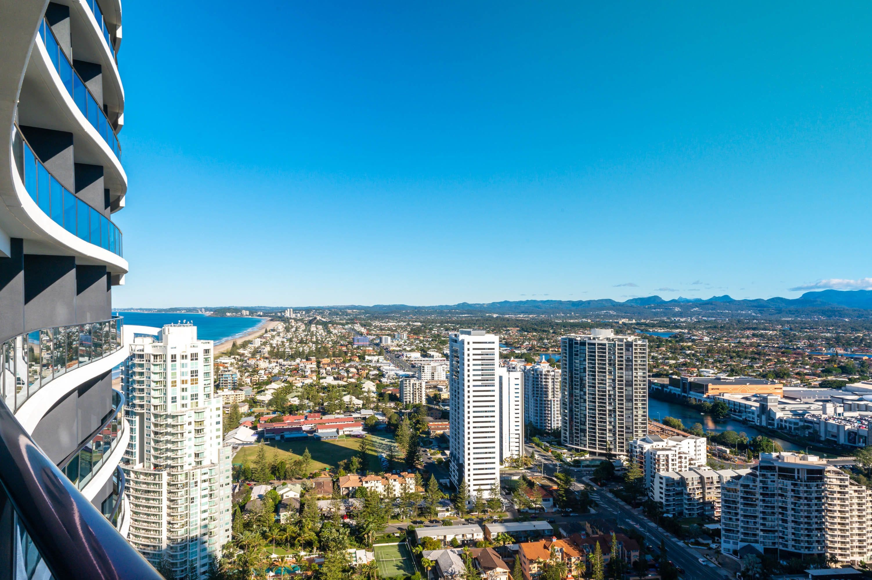 A high-rise building with multiple balconies, a view of a coastal cityscape, and a river running through the city.